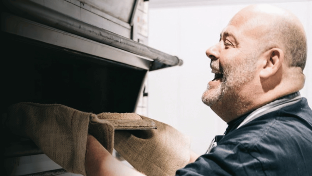 Master Baker Mark Bennett laughs whilst placing a baking tray in an oven