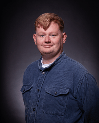 Portrait photo of George Turl standing side on, wearing a blue jacket